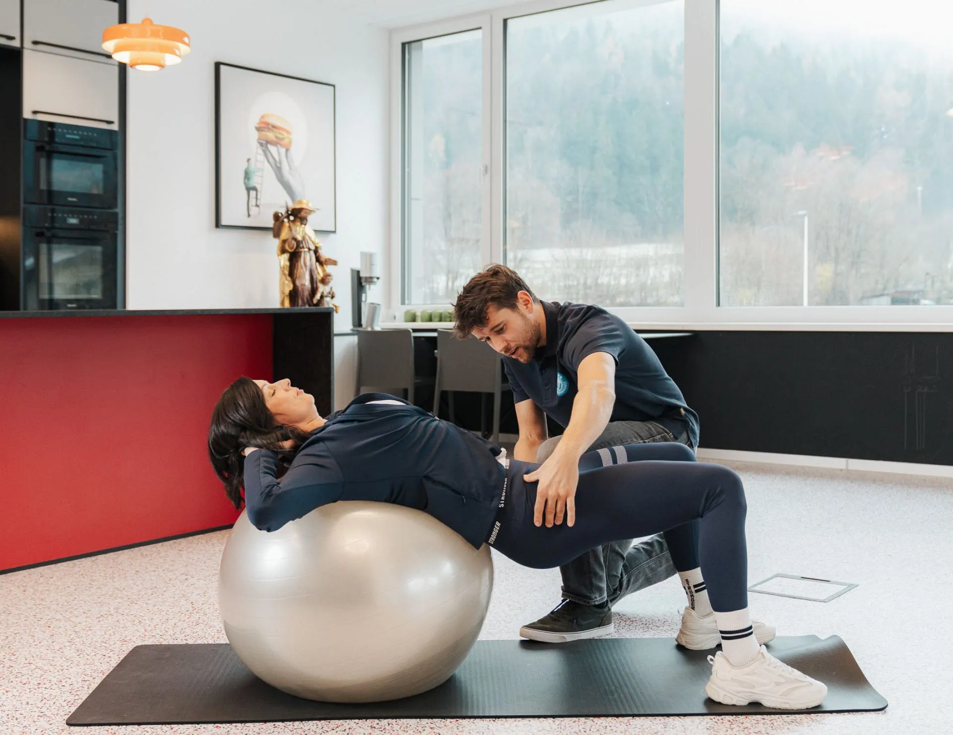 Mann unterstützt Frau auf einem Gymnastikball in modernem Raum